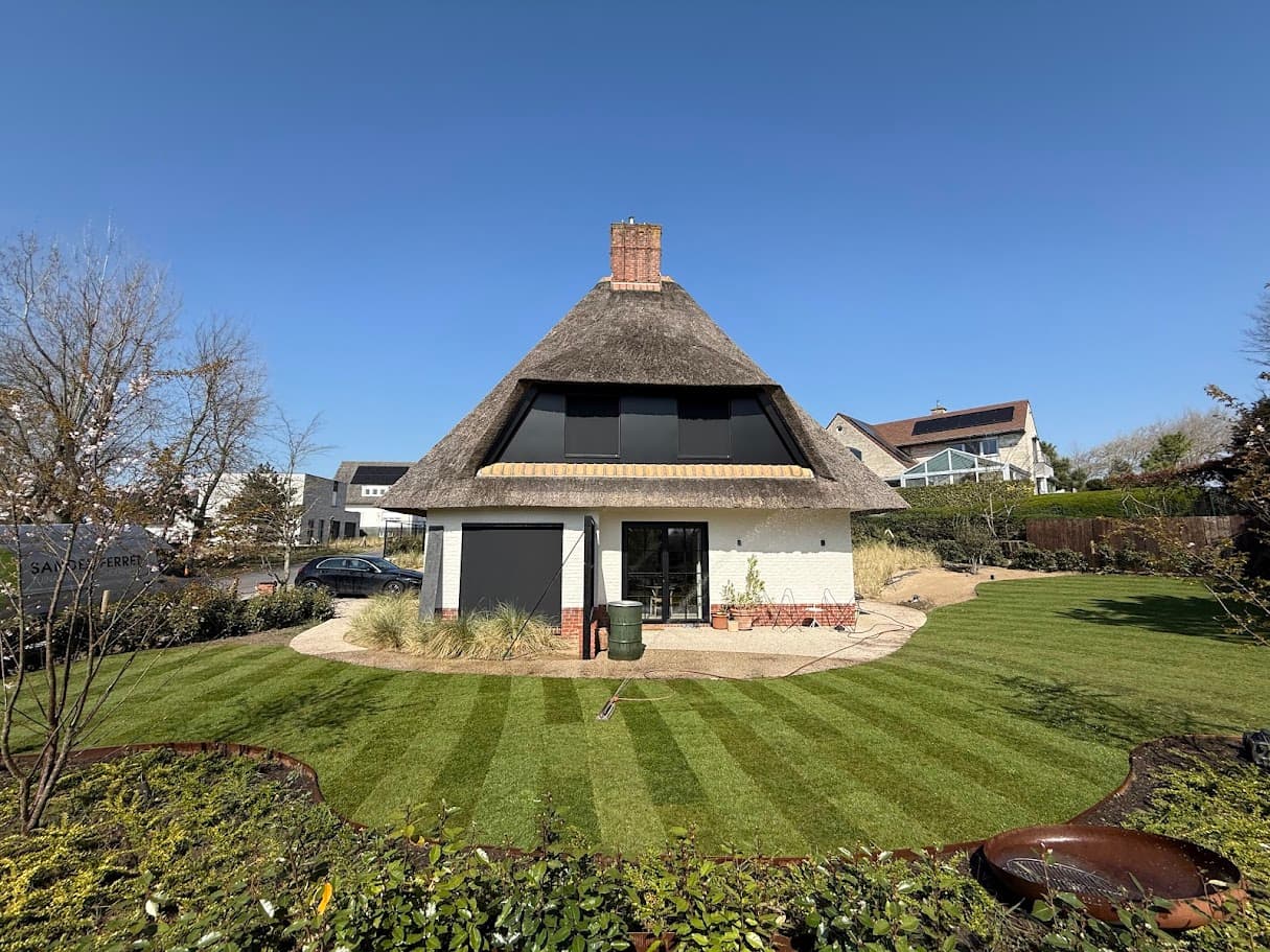Aangelegde tuin met gestreept gazon en cortenstalen boordranden rond een villa met rieten dak in Koksijde