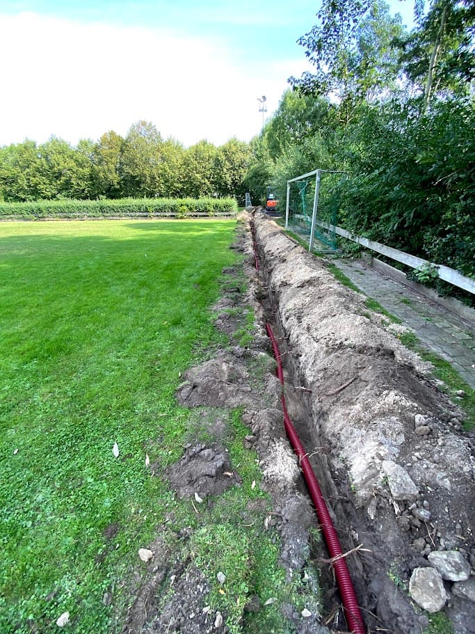 Sleuf met leiding langs een sportveld