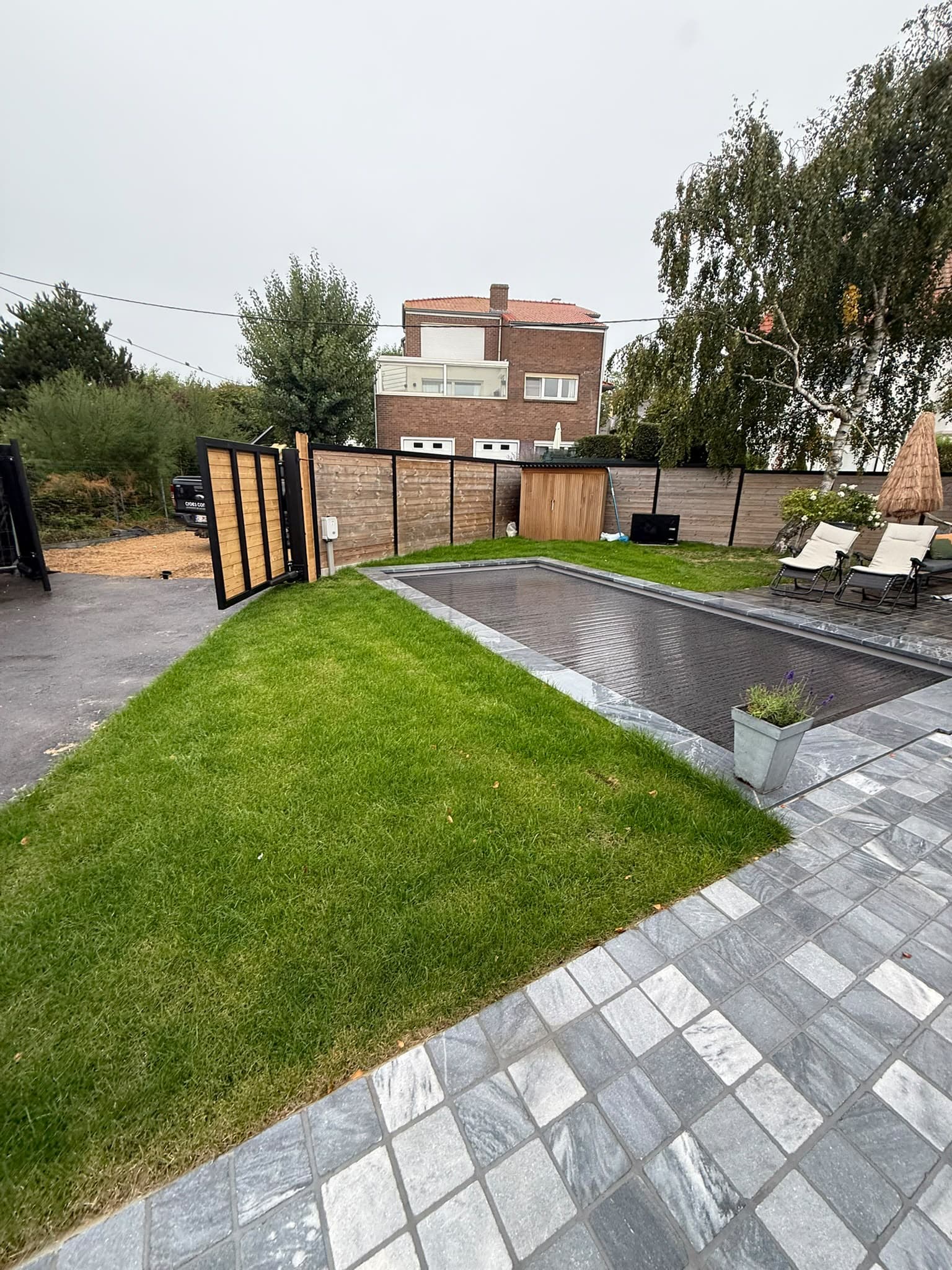 Nieuw gazon naast een tegelterras met ligzetels en houten omheining