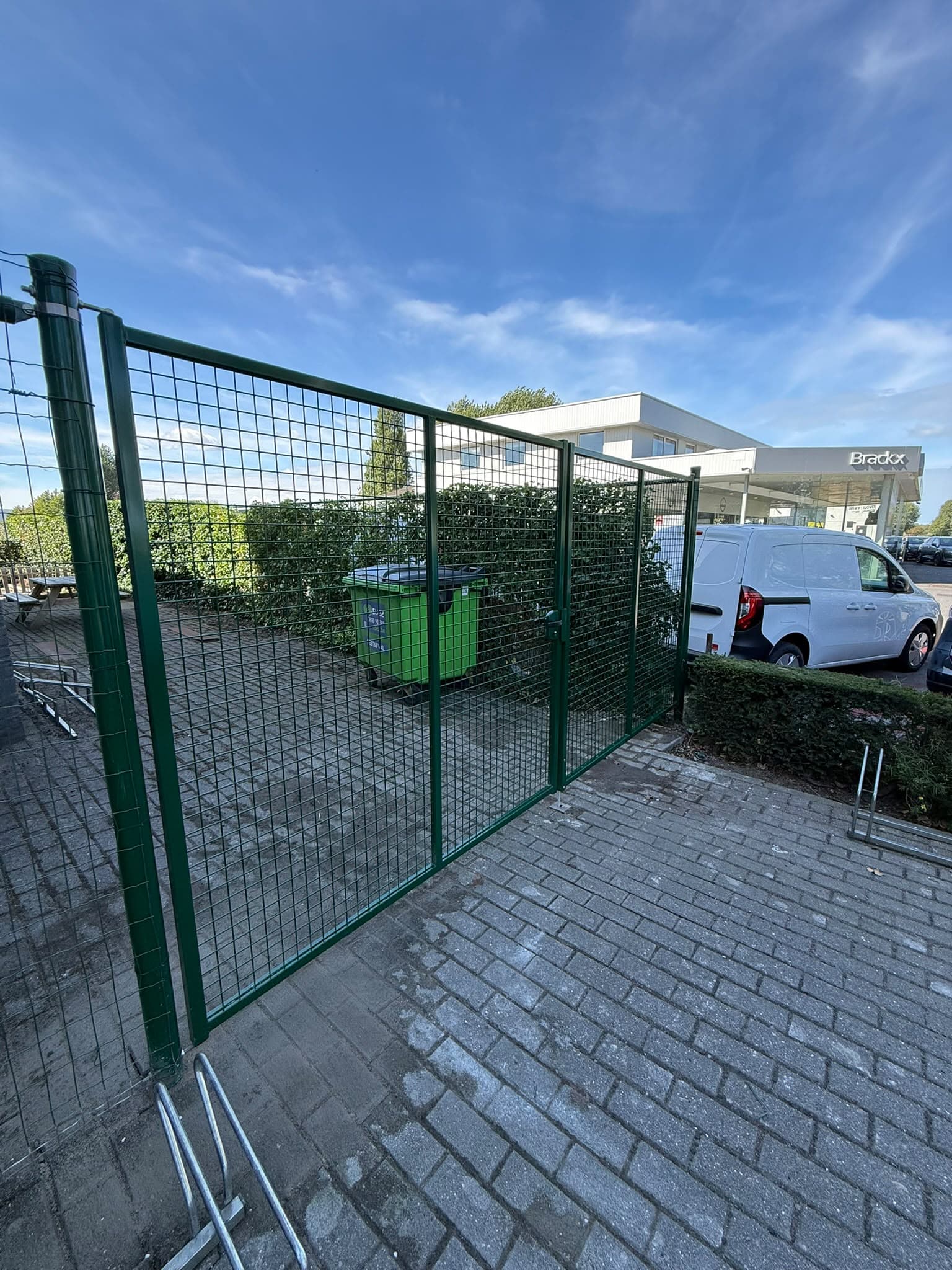 Groene draadpoort met afsluiting op een oprit in klinkers